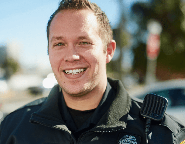 Police officer standing on the side of the street smiling.
